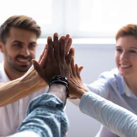 Happy diverse businesspeople giving high five, close up focus on people hands. Friendly multiracial company staff stacked their palms together symbol of friendship and good relations between coworkers