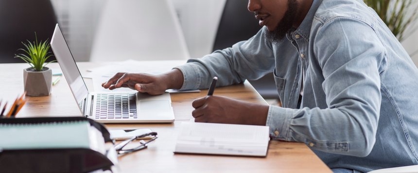 African American worker noting information from laptop in office