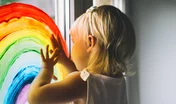 Little girl hands touch painting rainbow on window.